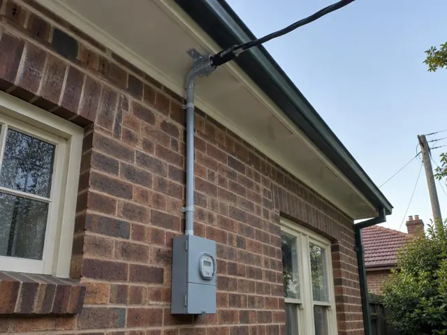Overhead service cable and point-of-attachment bracket on a brick house exterior in Roseville